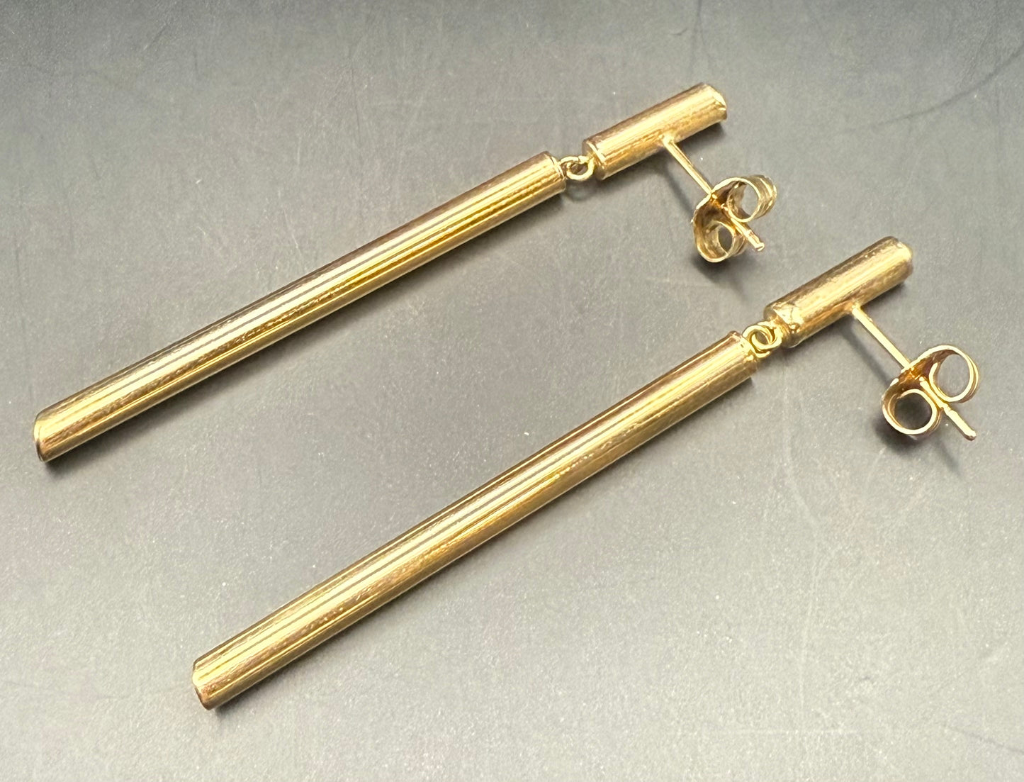 14K yellow gold tubular modernist earrings laid flat on solid background