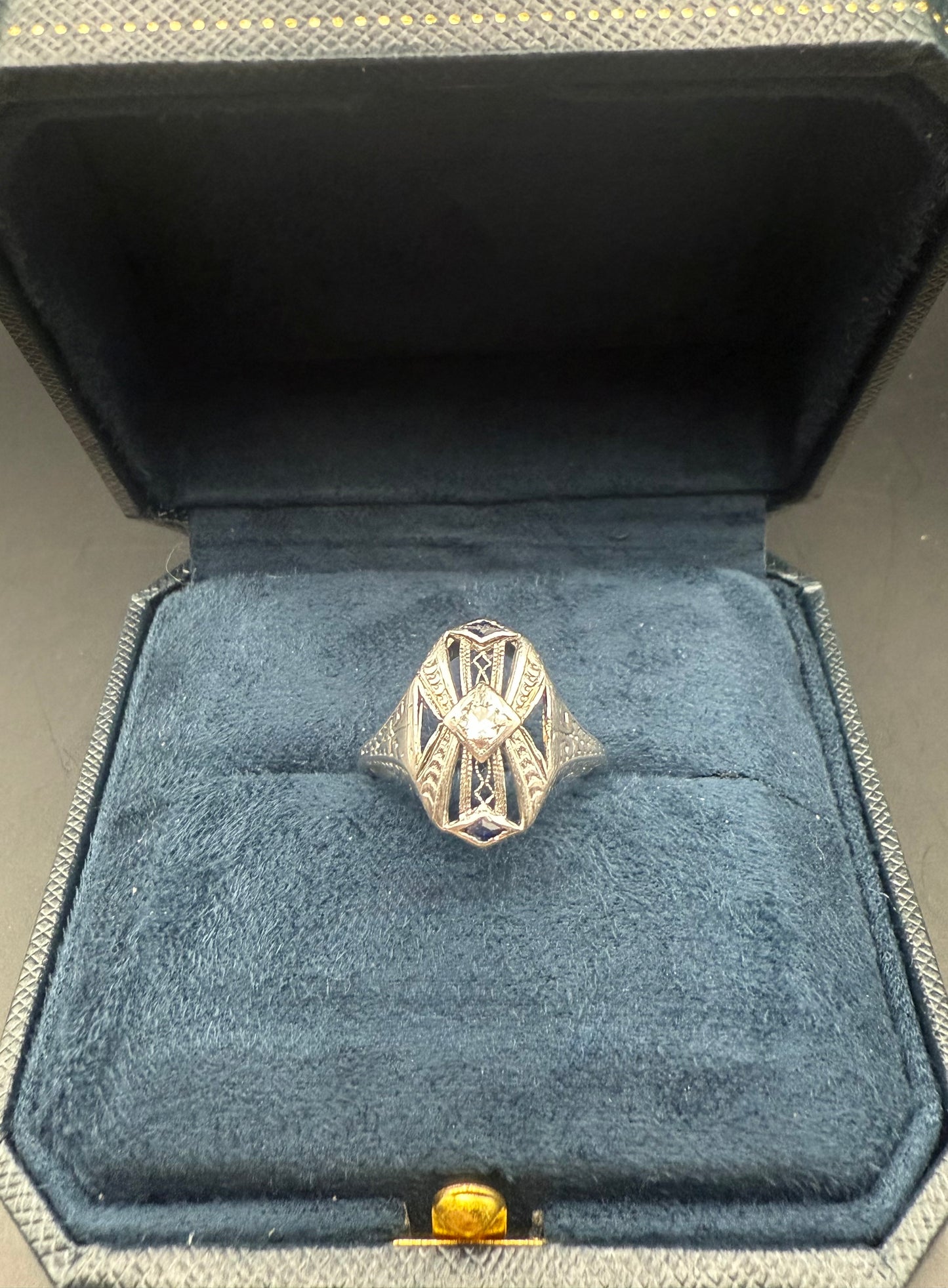 Angled view of 1920’s Art Deco diamond and sapphire filigree ring against light background