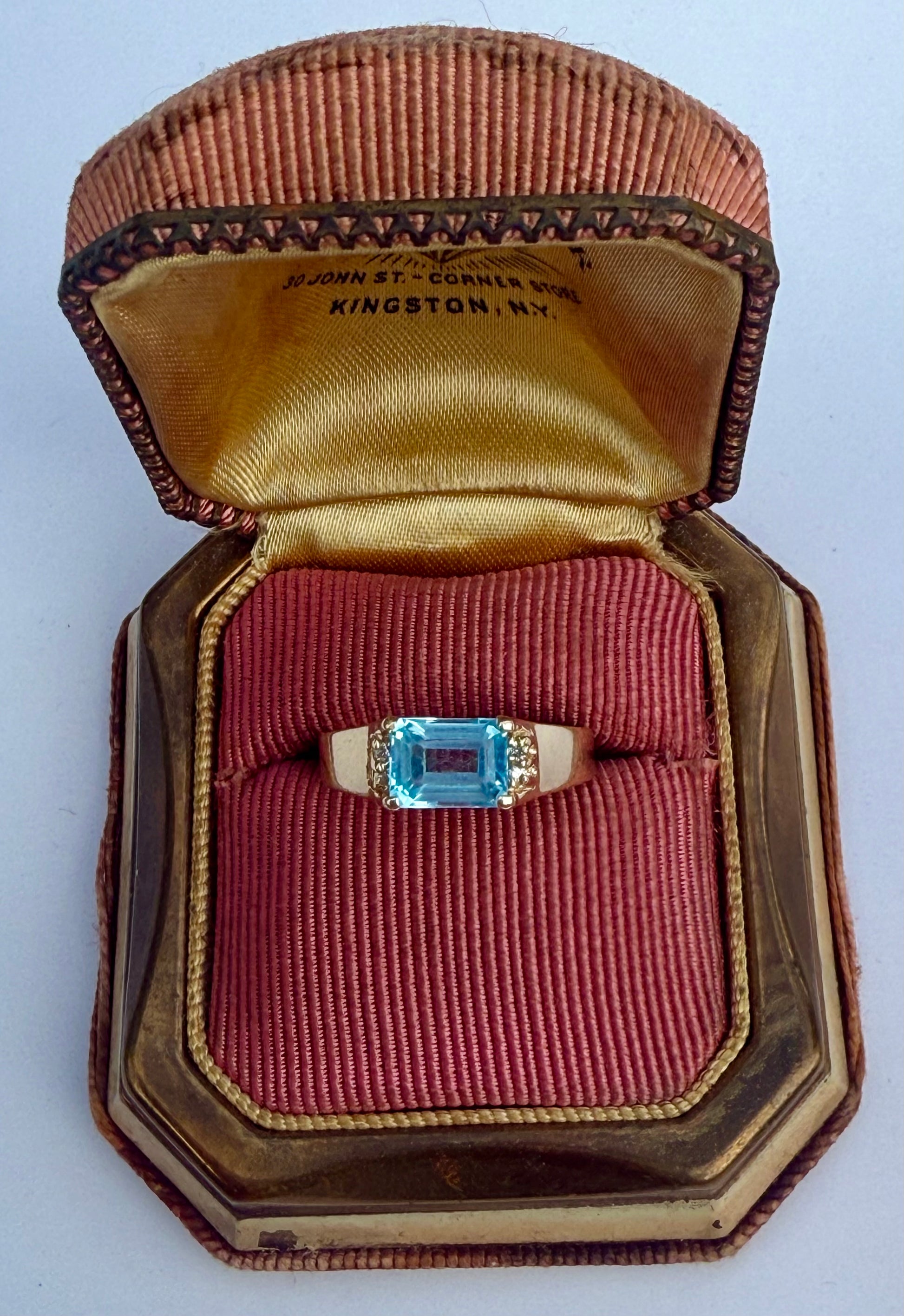 Close-up of 14K yellow gold ring featuring emerald-cut blue topaz and diamond accents, displayed in antique red jewelry box