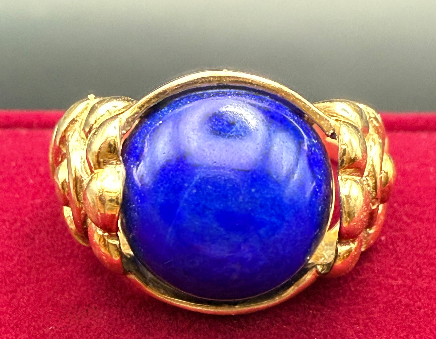 Close-up of vivid blue lapis cabochon in antique 10K gold floral ring, red background.