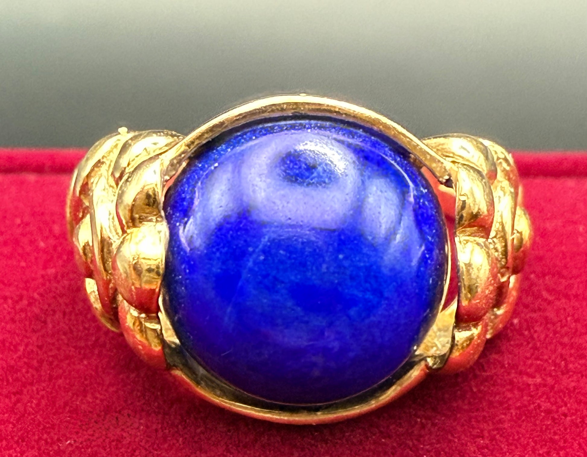 Close-up of vivid blue lapis cabochon in antique 10K gold floral ring, red background.