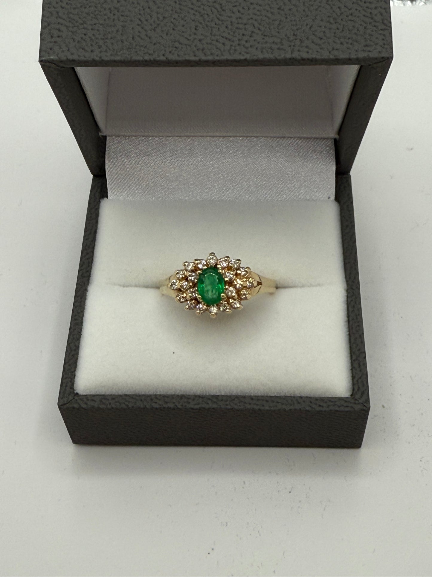 Emerald and diamond cluster ring displayed in gray presentation box