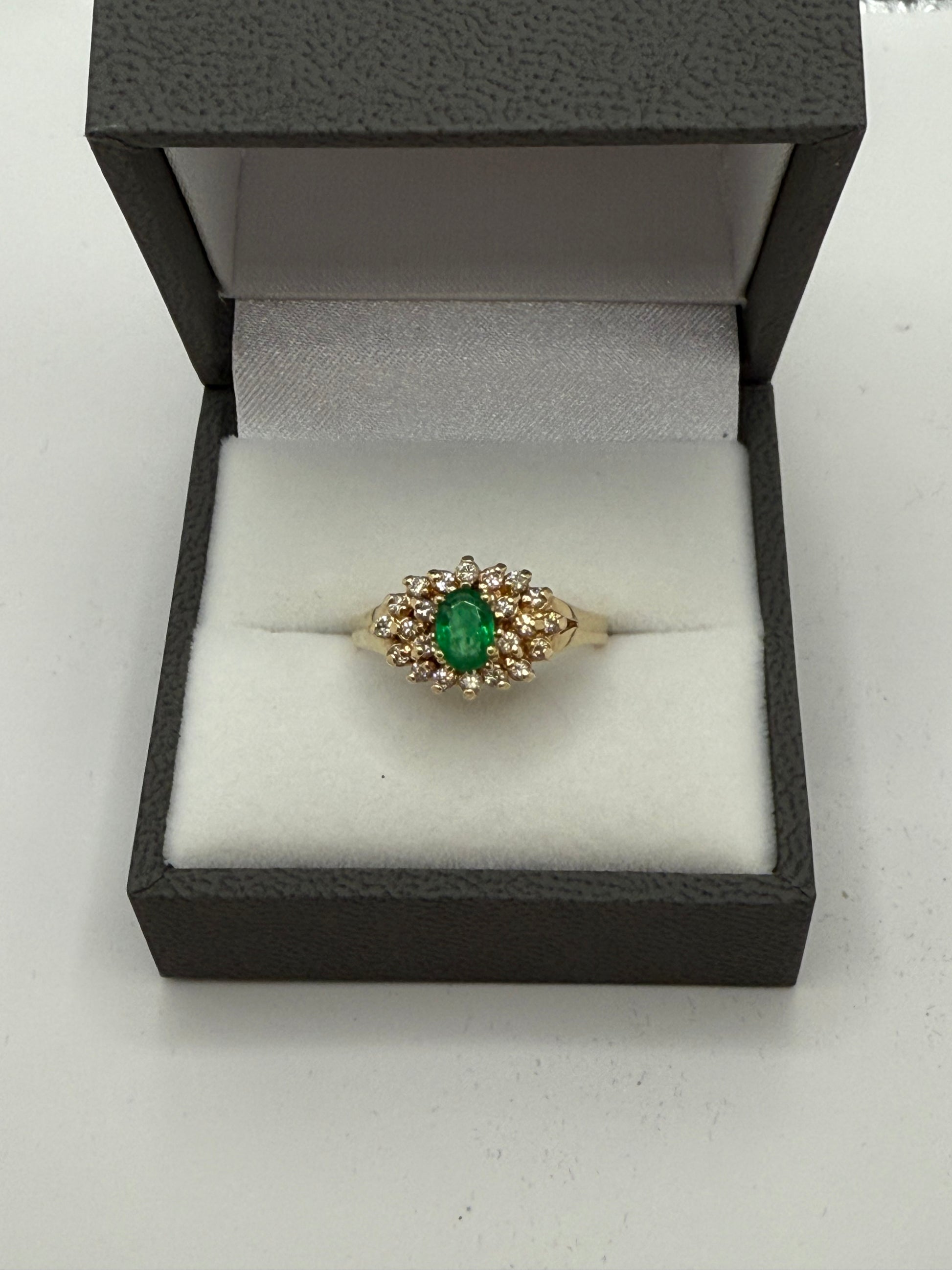 Emerald and diamond cluster ring displayed in gray presentation box