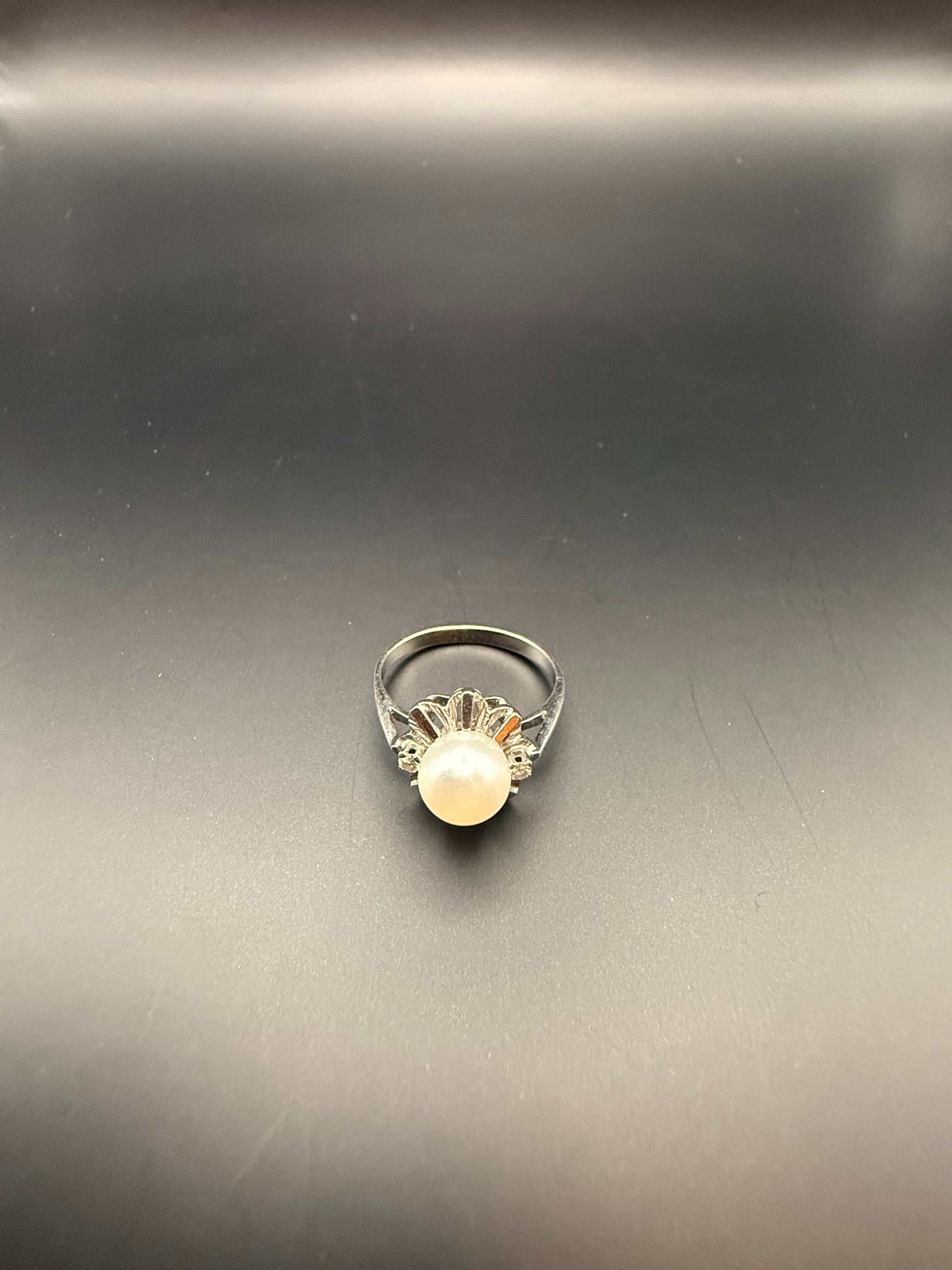 Estate 14K white gold ring with central white pearl and diamond accents in a flower motif, photographed on black background