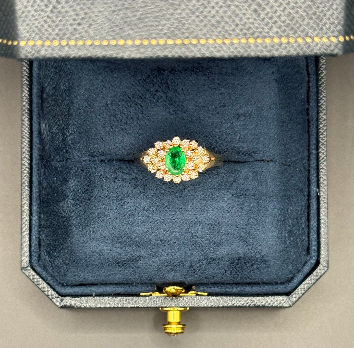 Overhead view of estate 14K yellow gold ring with oval emerald center and diamond halo cluster.