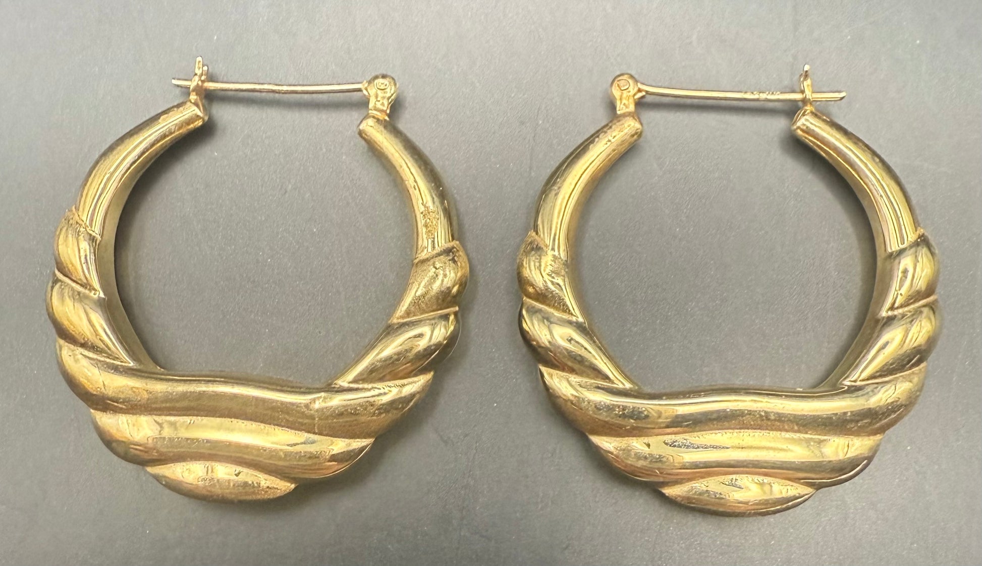 Pair of 14K yellow gold puffy hoop earrings displayed on textured background