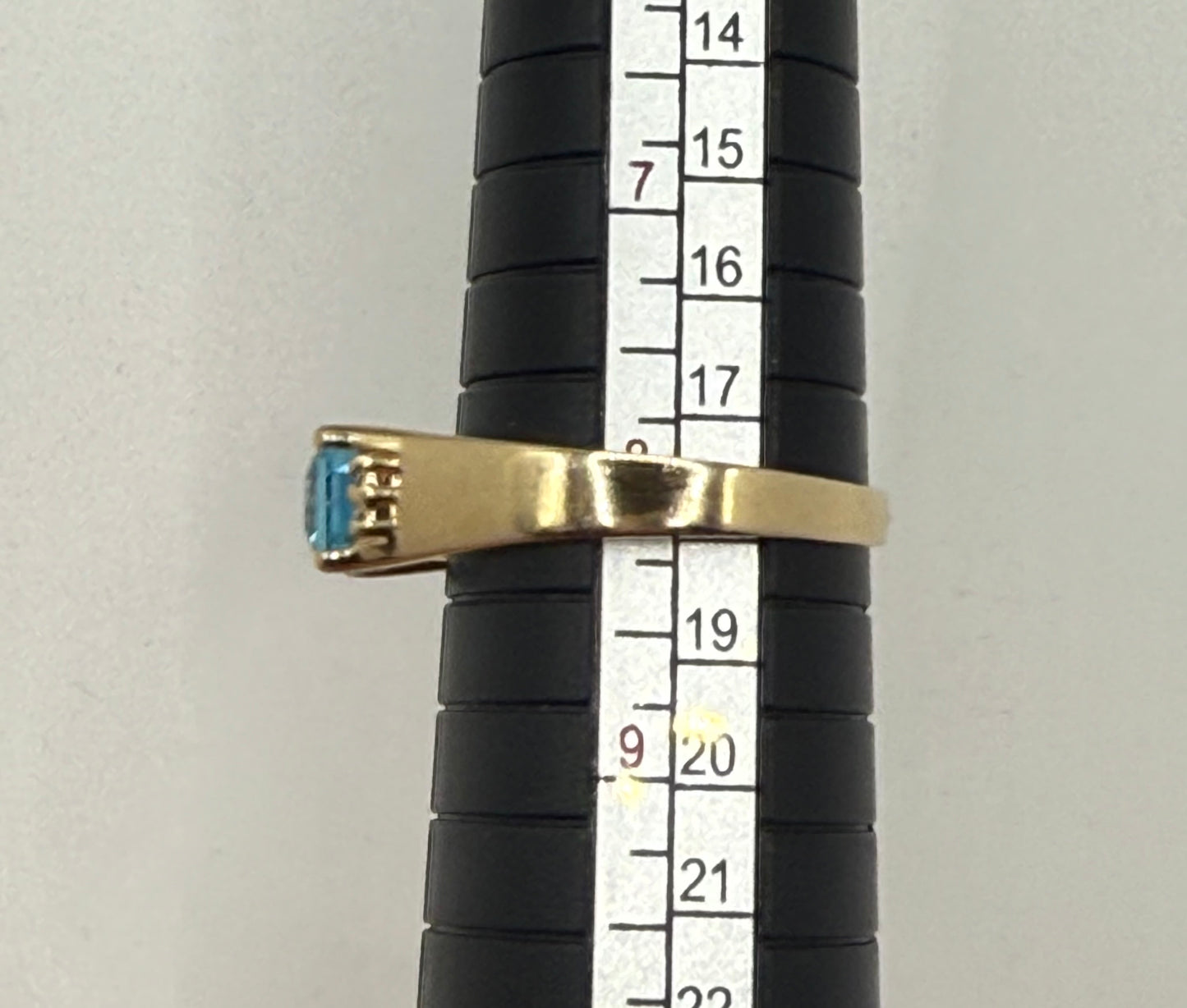 Ring on mandrel measuring size 8, showcasing sleek 14K yellow gold band and rectangular blue topaz.