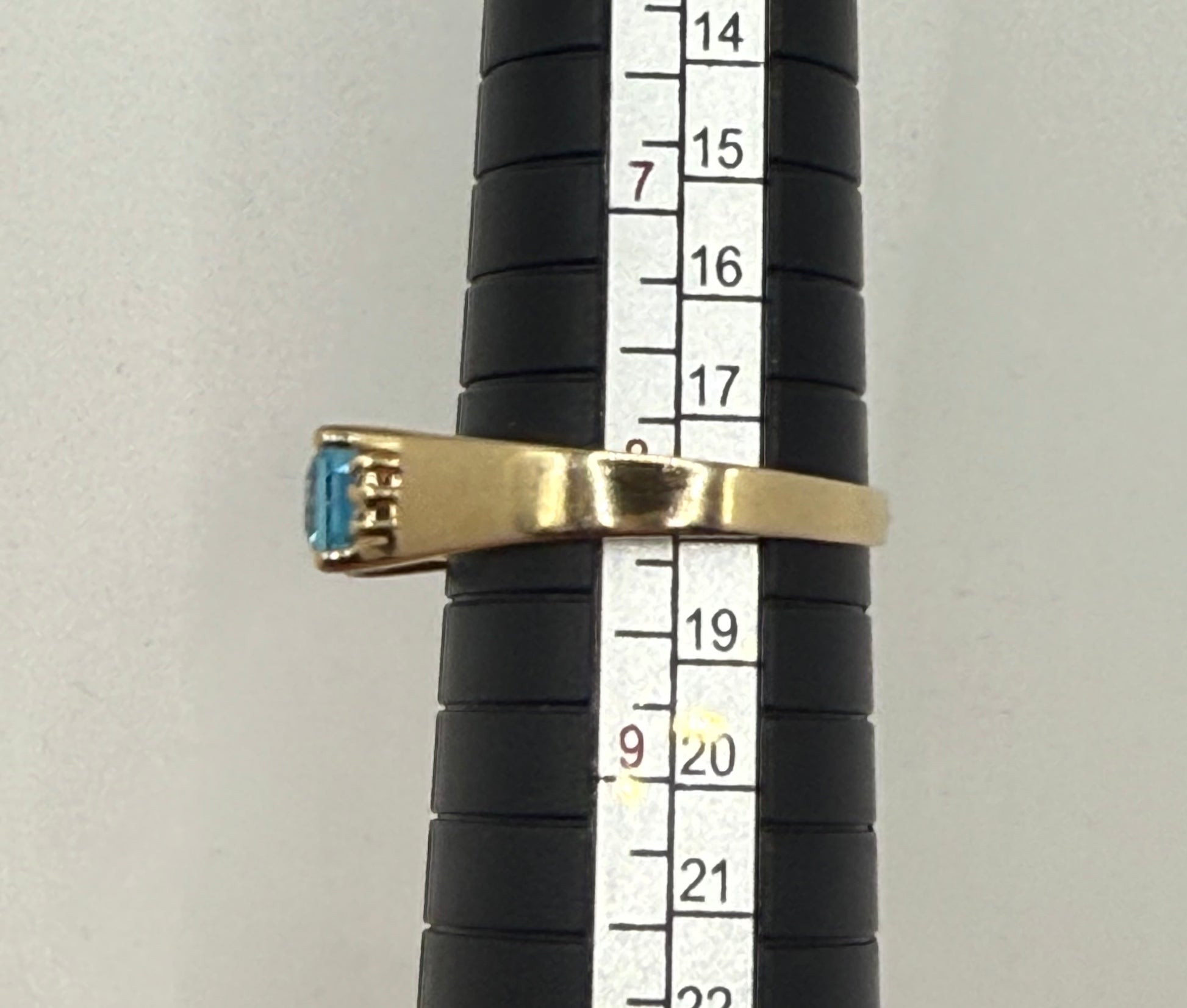 Ring on mandrel measuring size 8, showcasing sleek 14K yellow gold band and rectangular blue topaz.