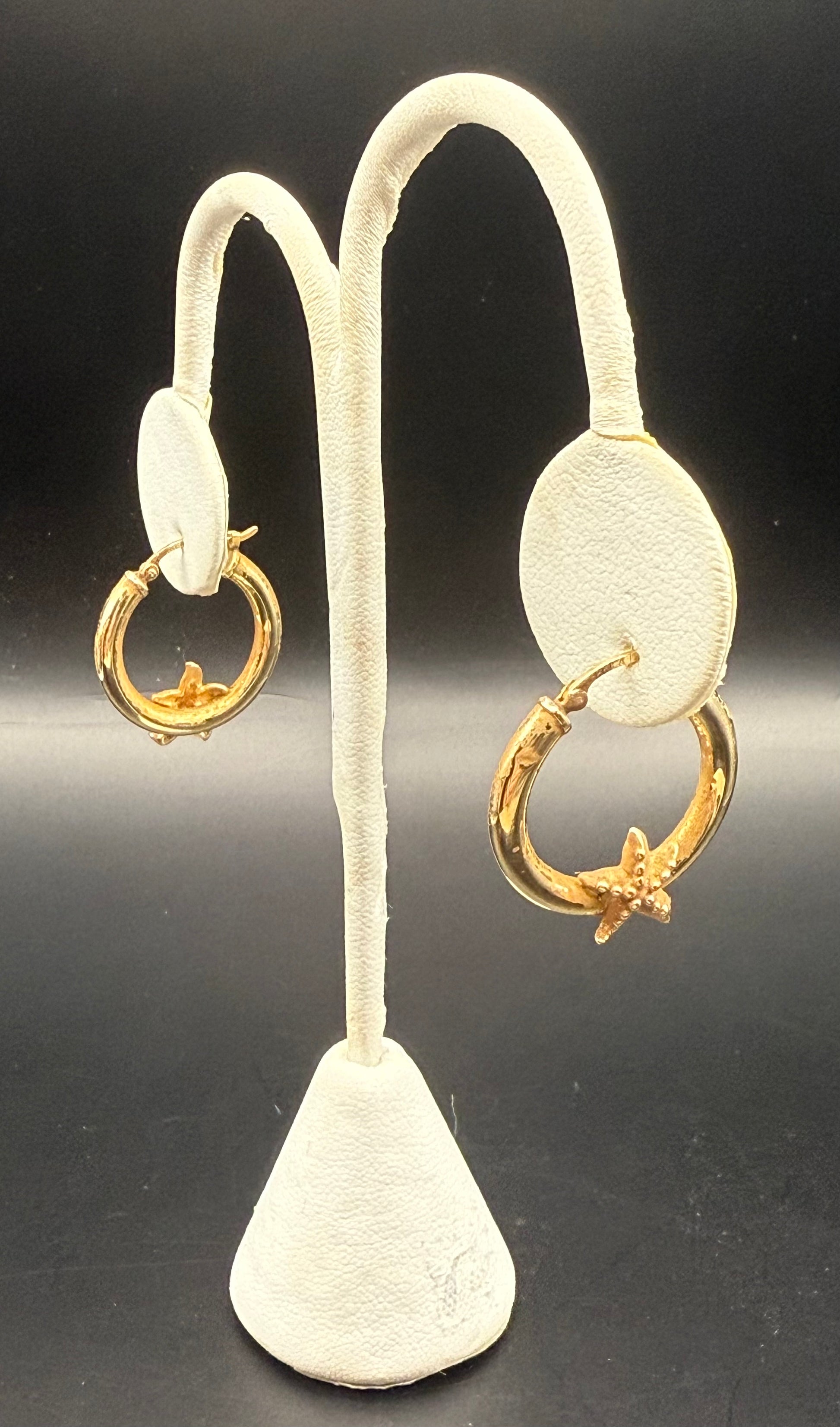 Starfish gold hoop earrings displayed on white earring stand