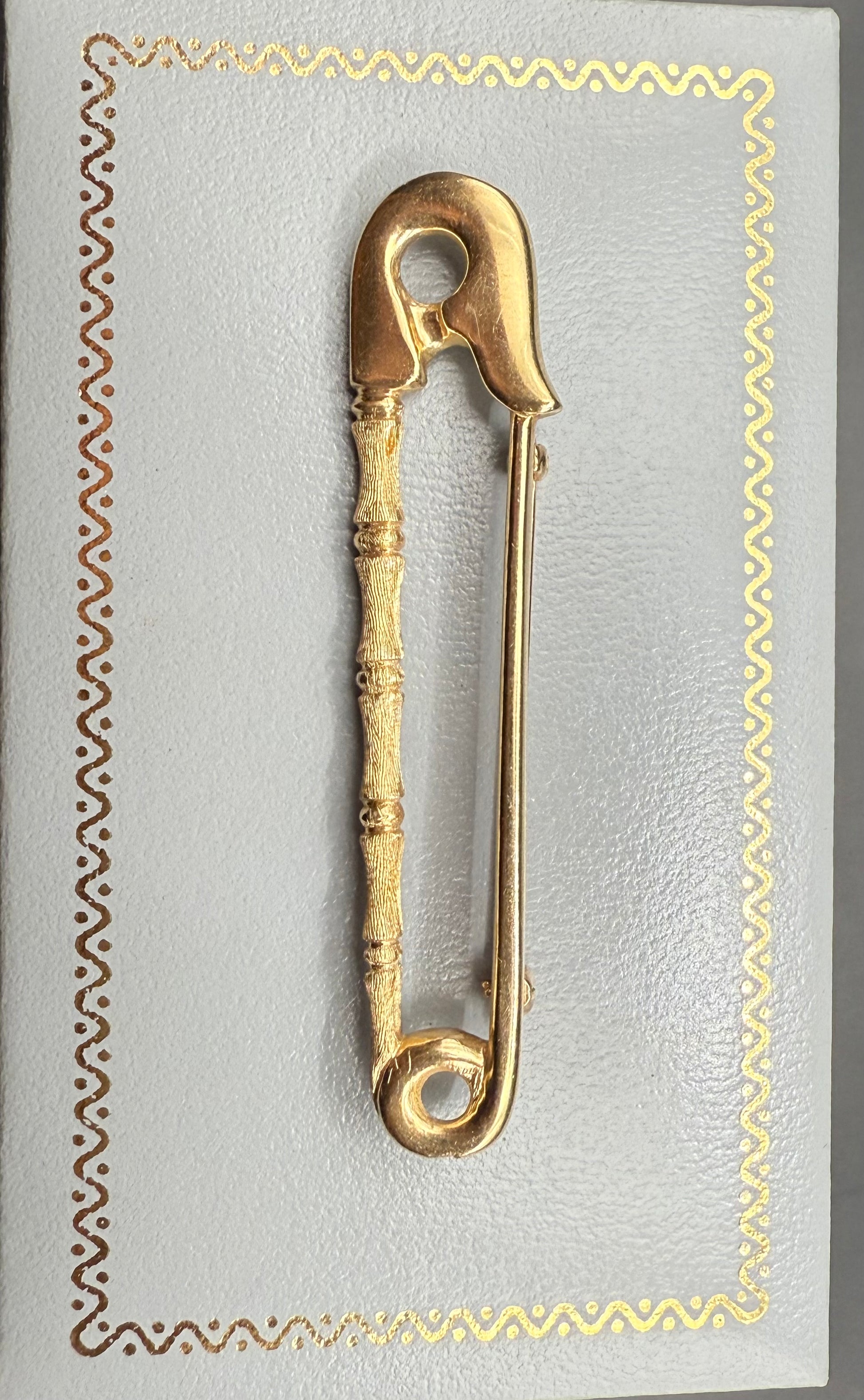 Vintage 14K yellow gold safety pin pendantbrooch with bamboo accent, displayed on decorative background