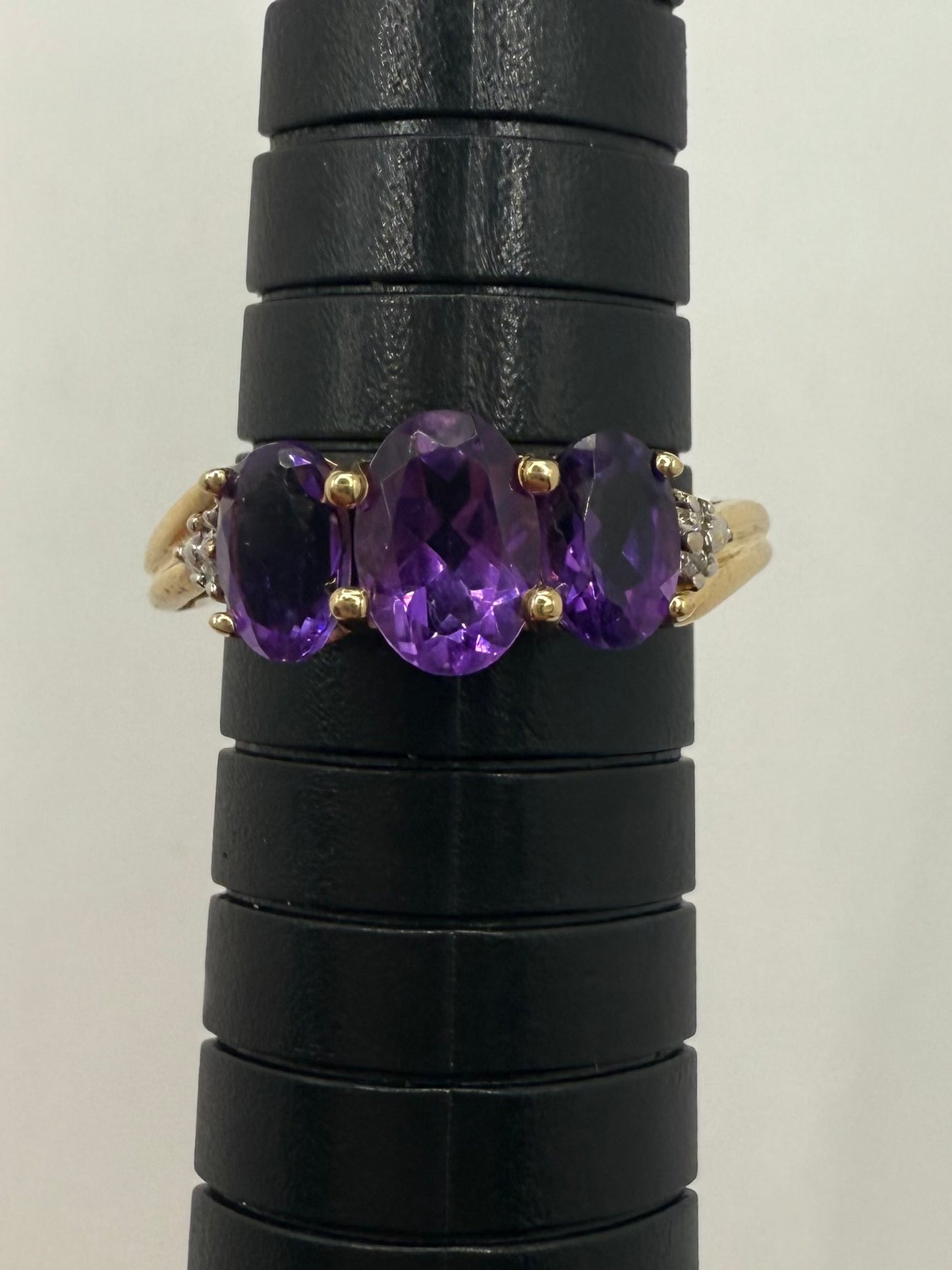 Vintage 3-stone amethyst ring in yellow gold with oval purple gemstones, trilogy design symbolizing past, present, and future.