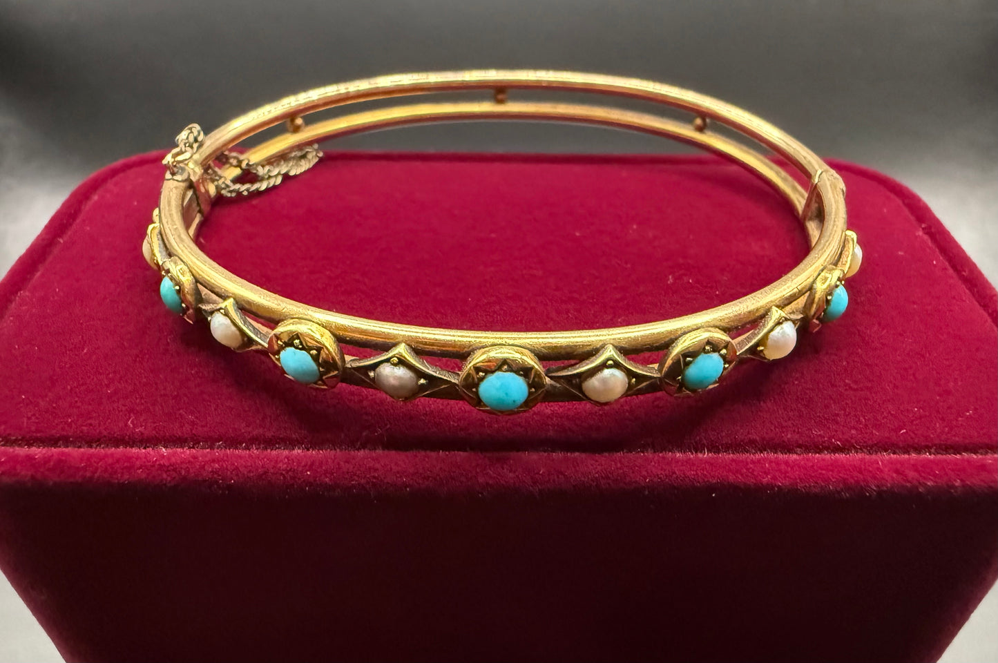 Front view of Victorian turquoise and pearl 14k rosy gold bangle bracelet on red velvet display