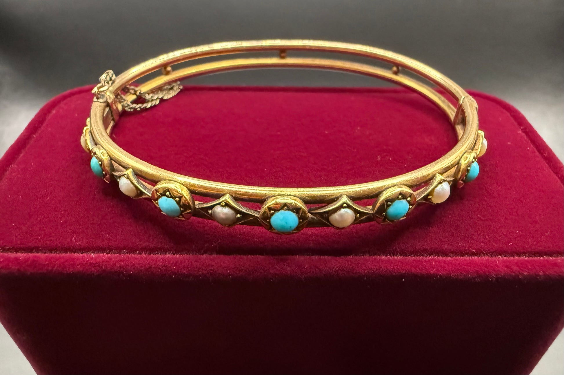 Front view of Victorian turquoise and pearl 14k rosy gold bangle bracelet on red velvet display